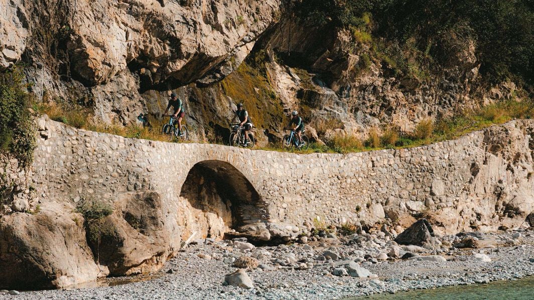 Gruppe von Radfahrern auf Canyon Gravelbikes überquert eine in Fels gehauene Steinbrücke, ideal zur Darstellung von Offroad-Fähigkeiten und Abenteuerpotenzial.